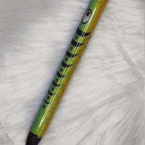 May include: A green and black pen with a fish design. The pen has a black tip and a silver clip.