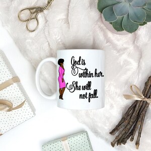 May include: White ceramic mug with a black and pink illustration of a woman and the text "God is within her. She will not fall."