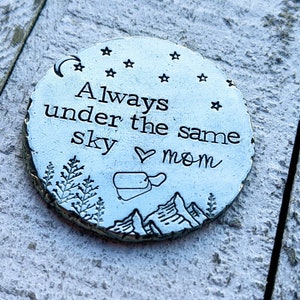 Peut inclure: Jeton rond en métal argenté avec le texte "Always under the same sky ♥ mom" et un croissant de lune, des étoiles, des montagnes et des arbres gravés à la surface.