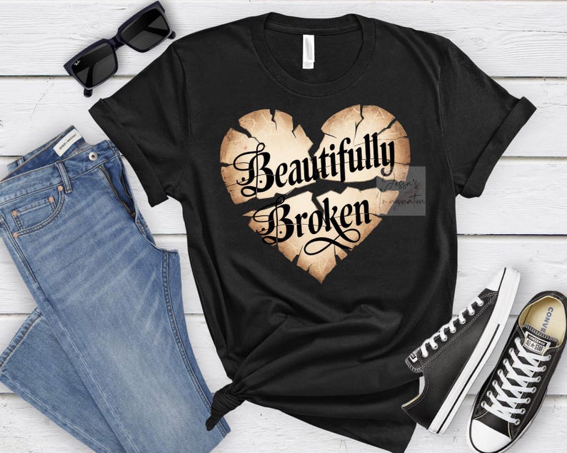 Peut inclure: T-shirt noir avec un motif de c&oelig;ur vieilli et l'inscription "Beautifully Broken". L'image pr&eacute;sente &eacute;galement un jean bleu, des lunettes de soleil noires et des baskets noires. Th&egrave;me : tenue d&eacute;contract&eacute;e.