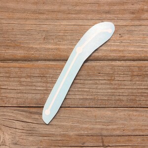 May include: A light blue boomerang with white markings. The boomerang is on a wooden surface.