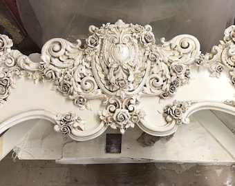 Puede incluir: Una cabecera blanca adornada con intrincados tallados florales y una cresta central. La cabecera está hecha de un material ligero y tiene un diseño delicado y femenino.