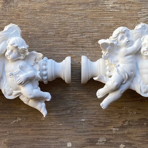 May include: Two white ceramic wall decor pieces featuring cherubs holding roses. Each piece has a cherub holding a rose with leaves and vines.