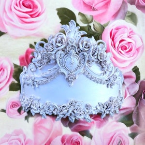 May include: White ornate decorative wall decor with a floral design. The decor is shaped like a crown and features intricate details and a raised center.