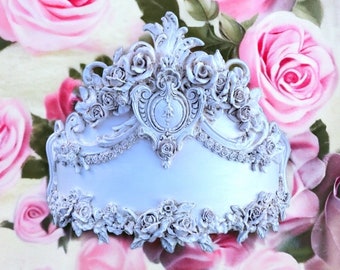 May include: White ornate decorative wall decor with a floral design. The decor is shaped like a crown and features intricate details and a raised centre.