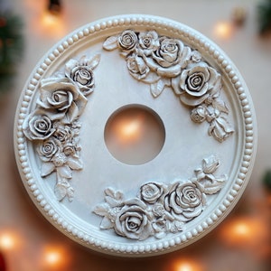 May include: A white ceiling medallion with a decorative floral design featuring raised roses and leaves. The medallion has a circular hole in the center.