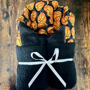 May include: A black hooded towel with a basketball print. The towel is tied with a white ribbon.