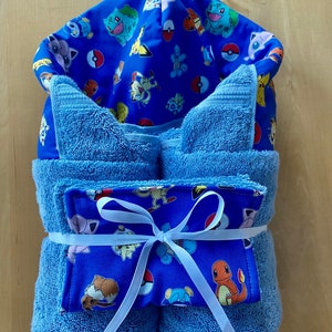 May include: Blue hooded towel with a Pokemon character print. The towel is rolled up and tied with a white ribbon.