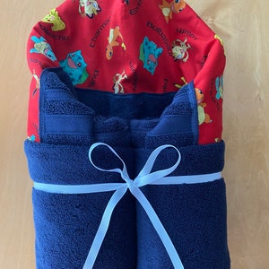 May include: A navy blue hooded towel with a white ribbon tied around it. The hood is made of red fabric with a Pokemon theme featuring characters like Pikachu, Bulbasaur, Charmander, and Squirtle.