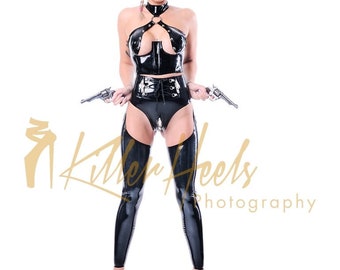 May include: A woman wearing a black latex outfit with a corset, garters, and thigh-high boots. She is holding two pistols and wearing a straw cowboy hat. The text "Killer Heels Photography" is visible in the background.