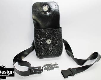 May include: A black leather phone bag with a textured finish and a black adjustable strap. The bag has a flap closure with a snap button. The strap has two metal buckles.