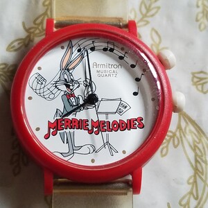 May include: Red plastic wristwatch with a white face featuring Bugs Bunny playing a musical instrument. The watch face says "Armitron Musical Quartz" and "Merrie Melodies".