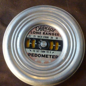 May include: A silver metal pedometer with a black and white dial that reads "Official Lone Ranger 35 25 Inch Stride 20 30" and "To Set Turn To 0 Pedometer".