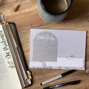 Puede incluir: Una hoja de trabajo de estudio bíblico gris y blanca con las palabras "Bible Study" en una fuente decorativa. La hoja de trabajo tiene secciones para el pasaje bíblico, el contexto, las principales conclusiones y los pasos a seguir. Hay dos bolígrafos negros sobre una superficie de madera junto a la hoja de trabajo.