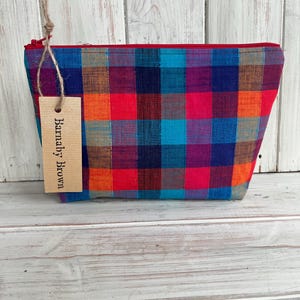 Può includere: Una pochette con cerniera a quadri rossi, blu, arancioni e viola con un'etichetta marrone che dice "Banally Brown".