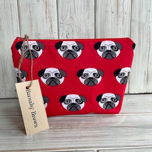 May include: Red zippered pouch with a repeating pattern of pug faces. The pouch has a brown tag that says "Barnaby Brown".