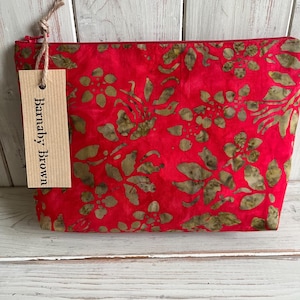 May include: A red zippered pouch with a floral pattern in shades of green and brown. The pouch has a tag that reads "Barnaby Brown". The bag is made of fabric and is likely used for cosmetics or small items.
