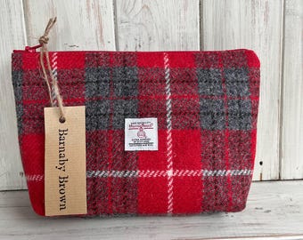 Könnte beinhalten: Rote und graue karierte Reißverschlusstasche mit einem braunen Etikett, auf dem "Handmade by Brown" steht. Das Etikett ist mit einer Schnur an der Tasche befestigt. Die Tasche ist aus Harris Tweed, einem hochwertigen Wollstoff aus Schottland.