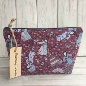 May include: A burgundy zippered pouch with a repeating pattern of women in traditional Japanese clothing, fans, and flowers. The pouch has a brown tag attached with the text "Barnaby Brown" written on it.
