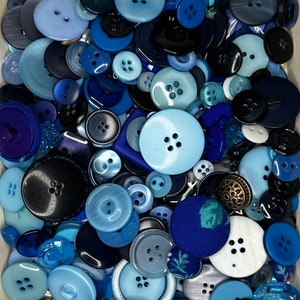 Op de afbeelding: Een verzameling blauwe en zwarte knopen in verschillende maten en stijlen. De knopen zijn gemaakt van plastic, metaal en stof.