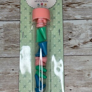 May include: A clear plastic tube with a pink lid filled with colorful point protectors. The label reads "100% Cute Point Protectors by Lori Holt of Bee in my Bonnet".