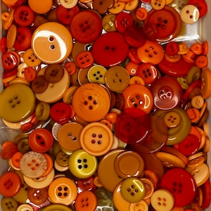 Op de afbeelding: Een verzameling van verschillende knopen in verschillende tinten oranje, bruin en geel. De knopen zijn gemaakt van plastic en hebben een gladde, glanzende afwerking.