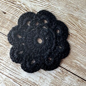 Puede incluir: Dos posavasos de ganchillo de color negro. Los posavasos están hechos de un hilo grueso y texturizado y tienen un diseño delicado e intrincado.