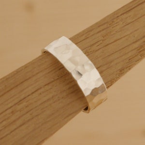 May include: A silver hammered band ring. The ring is thick and has a textured surface.