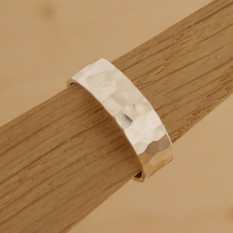 May include: A silver hammered band ring. The ring is thick and has a textured surface.