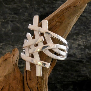 Könnte beinhalten: Ein silberner Ring mit einem geflochtenen Design. Der Ring besteht aus mehreren Silberbändern, die miteinander verflochten sind, um ein komplexes Muster zu erzeugen.