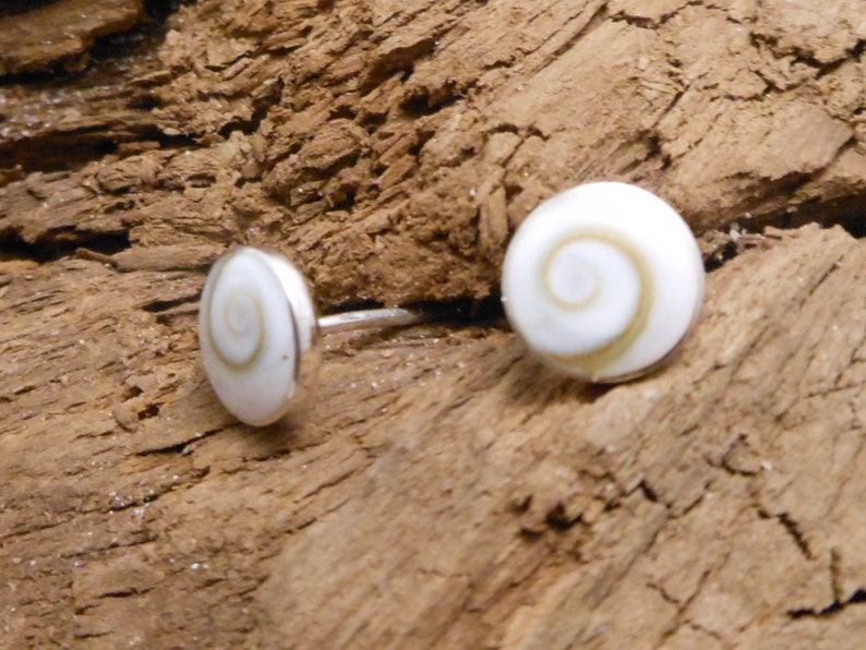 May include: A pair of silver stud earrings with white and brown shell inlays. The shell inlays have a spiral pattern.