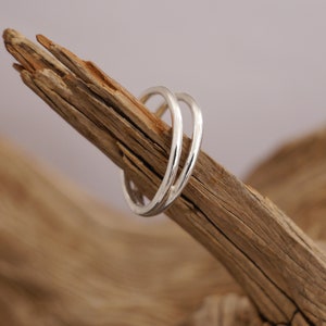 Könnte beinhalten: Zwei silberne Ringe, die übereinander liegen und auf einem Stück Treibholz ruhen.