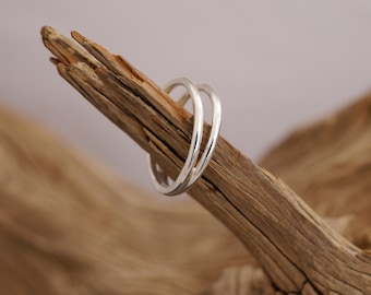 May include: Two silver rings stacked on top of each other, resting on a piece of driftwood.