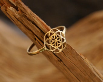 Puede incluir: Un anillo de oro con un diseño de flor geométrico. El anillo está sobre una pieza de madera.