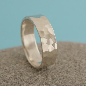 May include: A silver hammered band ring. The ring is wide and has a textured surface.