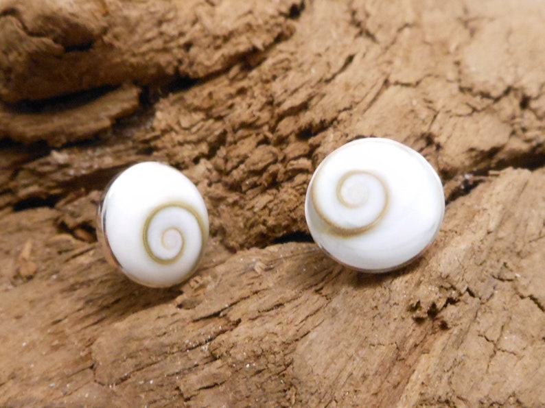 May include: A pair of silver earrings with white shell cabochons featuring a brown spiral pattern.
