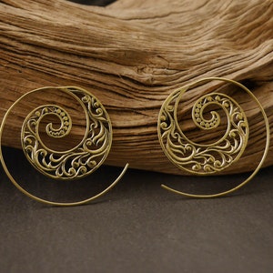 May include: A pair of gold-toned spiral earrings with a delicate floral design. The earrings are made of metal and have a hoop style.