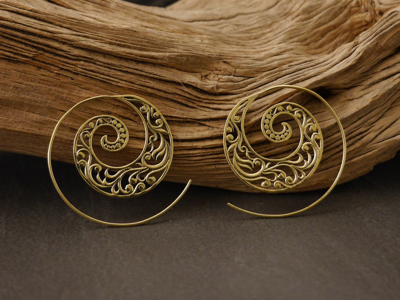 May include: A pair of gold-toned spiral earrings with a delicate floral design. The earrings are made of metal and have a hoop style.