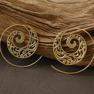 May include: A pair of gold-toned spiral earrings with a delicate floral design. The earrings are made of metal and have a hoop shape.