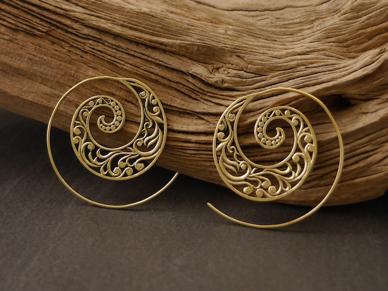 May include: A pair of gold-toned spiral earrings with a delicate floral design. The earrings are made of metal and have a hoop shape.