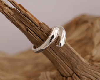 May include: A silver ring with a unique, curved design. The ring is smooth and polished, and it is shown on a piece of driftwood.