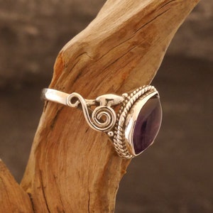 May include: A silver ring with an ornate design and a large, faceted amethyst gemstone.