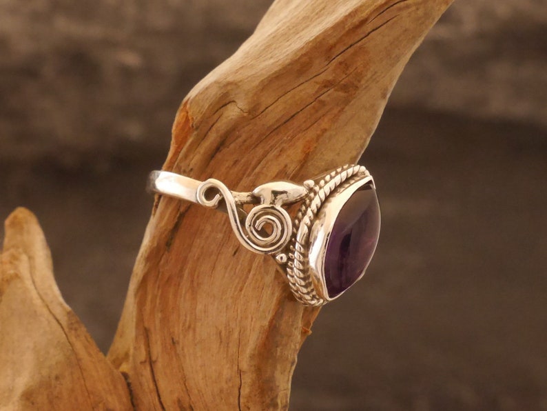 May include: A silver ring with an ornate design and a large, faceted amethyst gemstone.