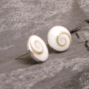 May include: A pair of silver stud earrings with white shell cabochons featuring a brown spiral design.