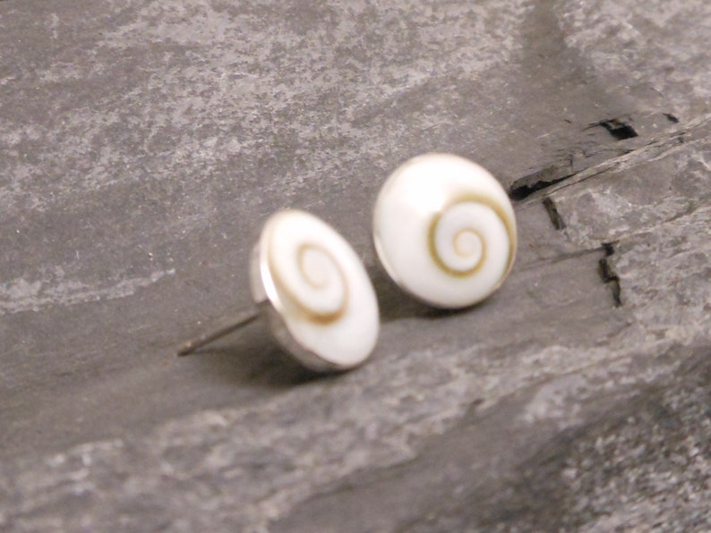 May include: A pair of silver stud earrings with white shell cabochons featuring a brown spiral design.