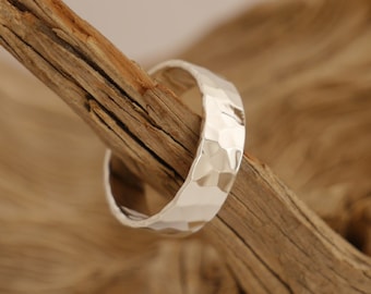 May include: A silver hammered ring with a wide band. The ring is sitting on a piece of driftwood.