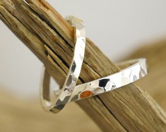 May include: Two silver hammered rings, stacked on top of each other, on a piece of driftwood.