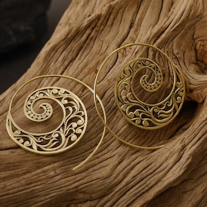 May include: A pair of gold-toned spiral hoop earrings with a delicate floral design. The earrings are made of metal and have a wire-like structure.