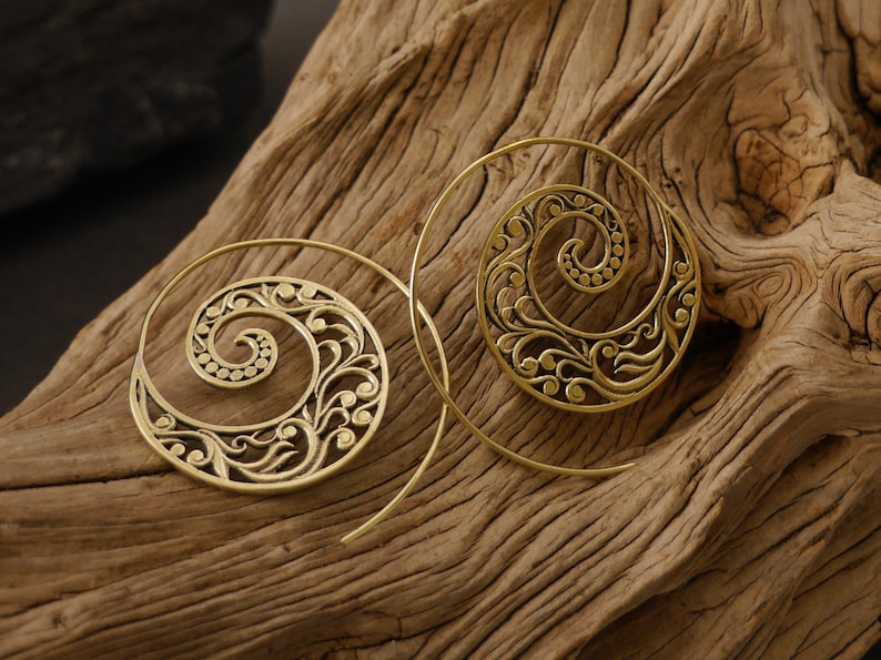 May include: A pair of gold-toned spiral hoop earrings with a delicate floral design. The earrings are made of metal and have a wire-like structure.