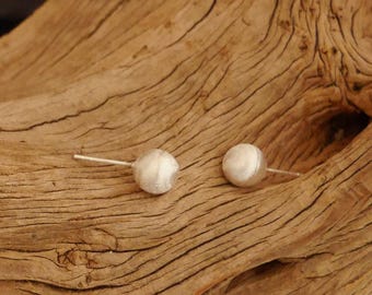 May include: A pair of silver stud earrings with a round, textured design. The earrings are displayed on a piece of driftwood.